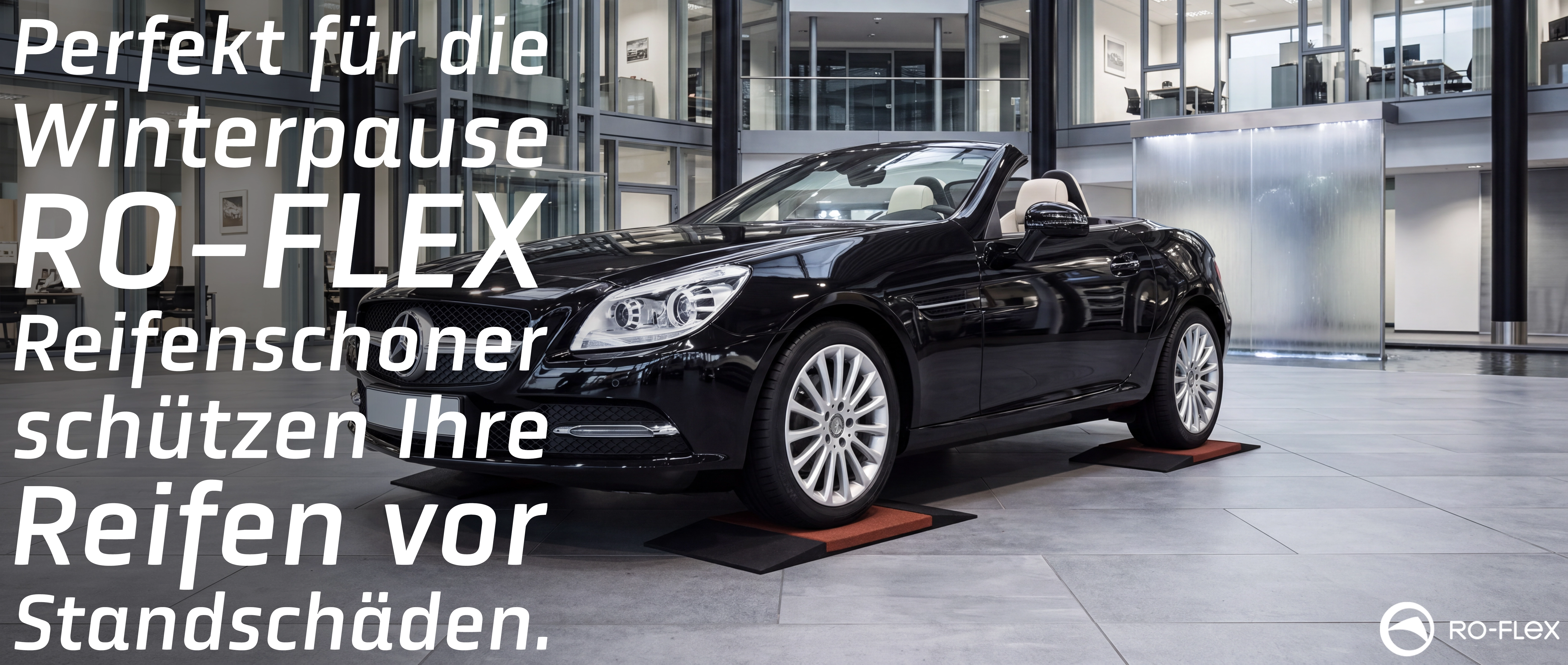 Schwarzer Mercedes-Benz SLK Cabrio steht in einer modernen Autohaus-Halle auf schwarzen und roten RO-FLEX Reifenschonern. Die Unterlagen schützen die Reifen vor Standschäden während der Winterpause. RO-FLEX-Logo unten rechts.
